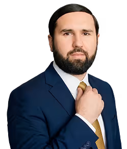 Man with dark hair and beard in a navy blue suit adjusting his yellow tie.