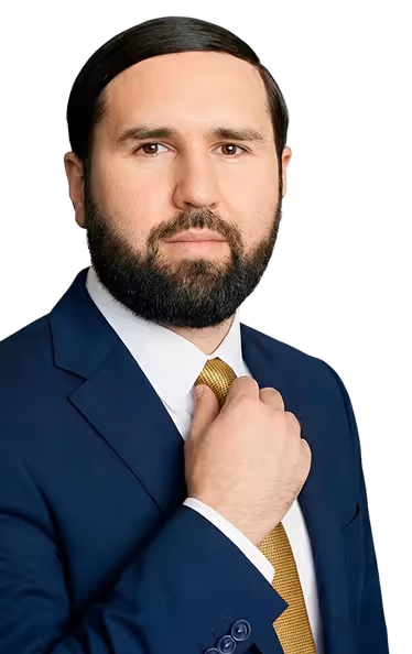 Man with dark hair and beard adjusting his gold tie, wearing a dark blue suit and white shirt.