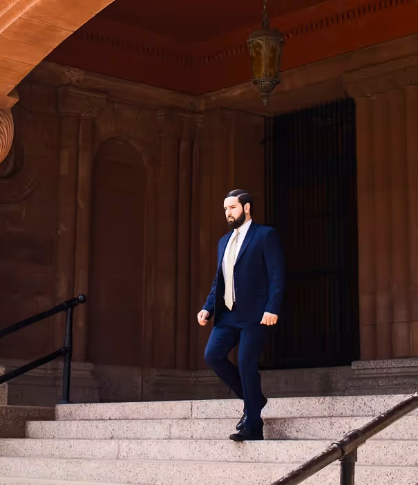 Man in a navy blue suit and light-colored tie walking down stone steps of a building with dark ornate architecture.